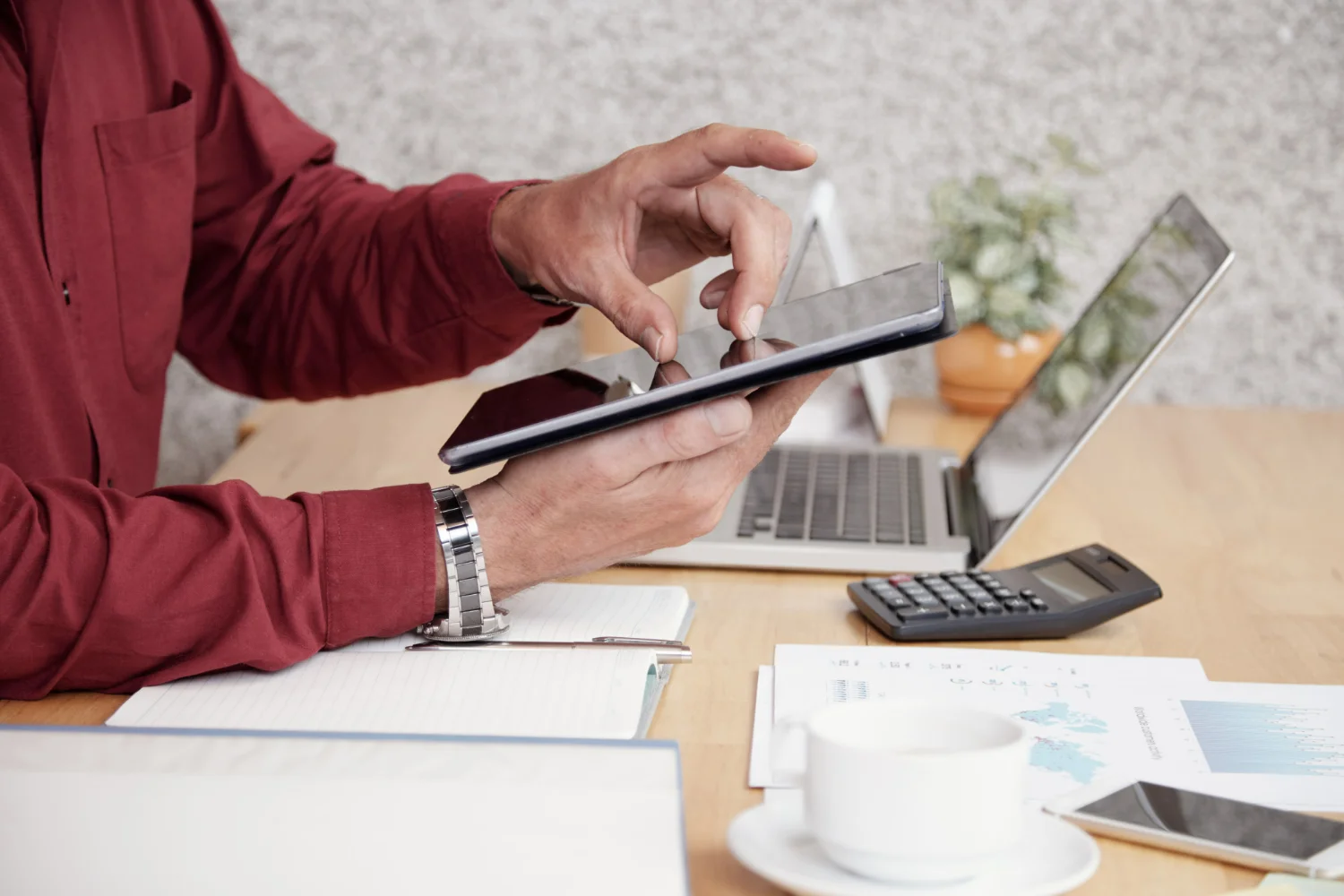 Homem de camisa vermelha com tablet na mão e calculadora na mesa fazendo balanço patrimonial